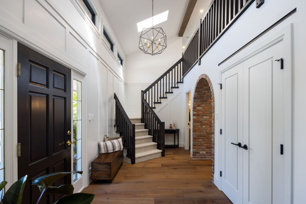 Mid-sized transitional medium tone wood floor, brown floor and wall paneling foyer photo in Vancouver with white walls and a black front door