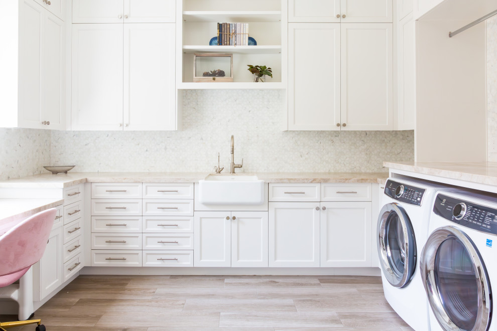 Inspiration for a large classic u-shaped utility room in Houston with white cabinets, white splashback, marble splashback, a side by side washer and dryer, beige worktops, a belfast sink, flat-panel cabinets, porcelain flooring and beige floors.