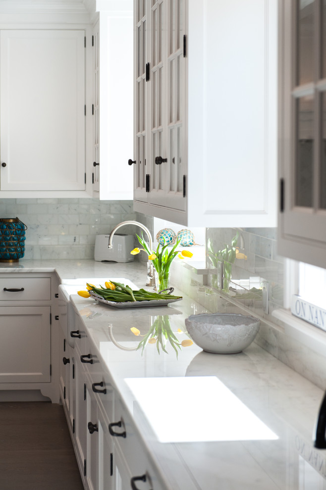 Inspiration for a large transitional l-shaped medium tone wood floor and brown floor eat-in kitchen remodel in Boston with a farmhouse sink, shaker cabinets, white cabinets, gray backsplash, paneled appliances, an island, marble countertops and marble backsplash