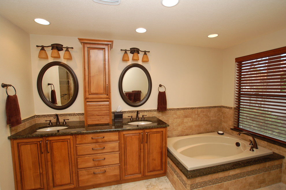 This is an example of a mid-sized traditional master bathroom in Boise with an undermount sink, raised-panel cabinets, medium wood cabinets, granite benchtops, a drop-in tub, a corner shower, brown tile, ceramic tile, beige walls and ceramic floors.
