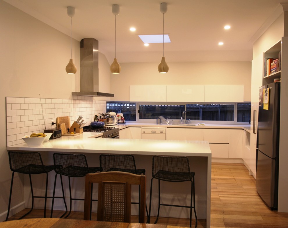 Inspiration for a contemporary u-shaped eat-in kitchen in Melbourne with an undermount sink, white splashback, subway tile splashback, stainless steel appliances, light hardwood floors, no island and white cabinets.