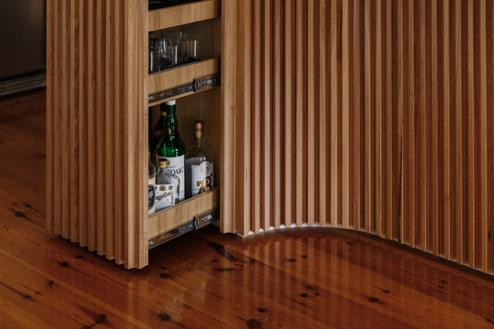 This is an example of a mid-sized midcentury l-shaped eat-in kitchen in Adelaide with an undermount sink, flat-panel cabinets, black cabinets, solid surface benchtops, grey splashback, stone slab splashback, panelled appliances, light hardwood floors, with island, brown floor and grey benchtop.