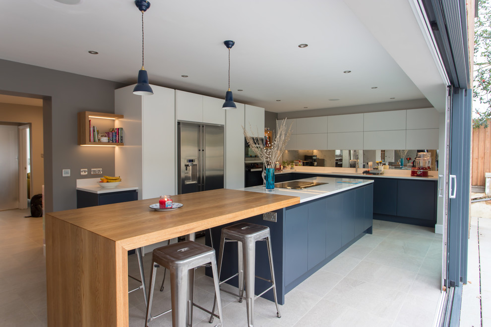 This is an example of a contemporary l-shaped eat-in kitchen in Hertfordshire with a drop-in sink, flat-panel cabinets, blue cabinets, quartzite benchtops, metallic splashback, mirror splashback, stainless steel appliances, porcelain floors, with island, white floor and white benchtop.