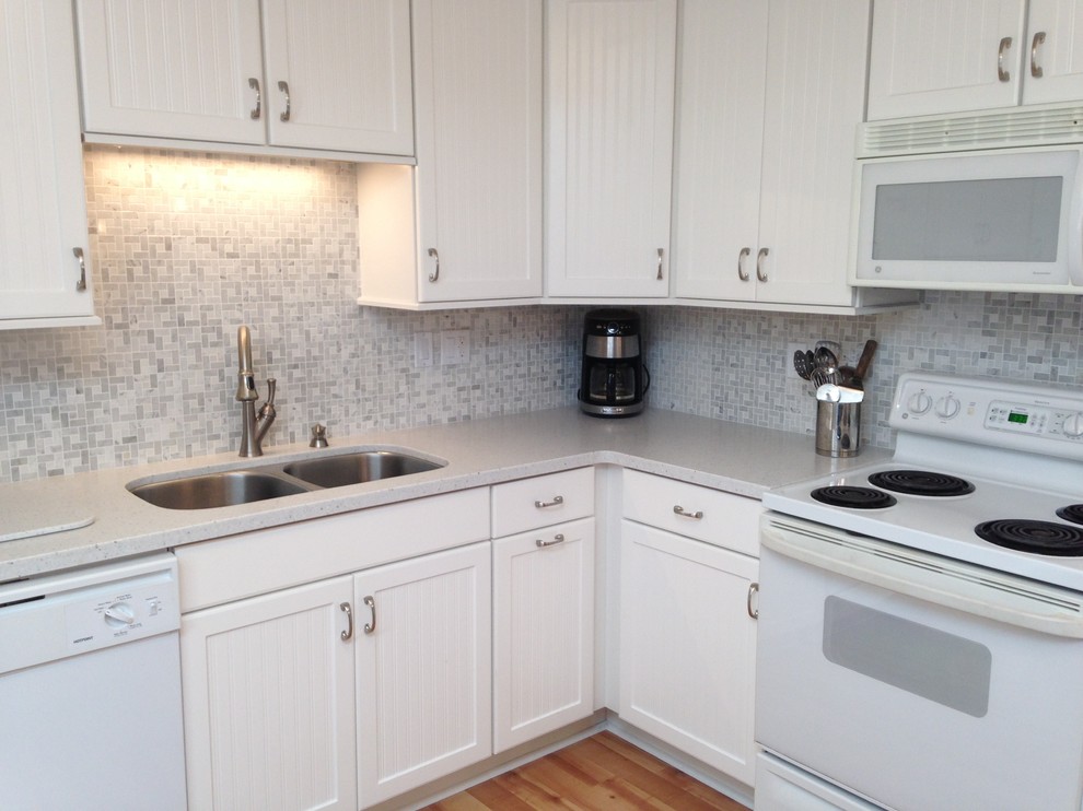 Eat-in kitchen - mid-sized coastal l-shaped eat-in kitchen idea with an undermount sink, beaded inset cabinets, white cabinets, solid surface countertops, gray backsplash, mosaic tile backsplash, white appliances and a peninsula