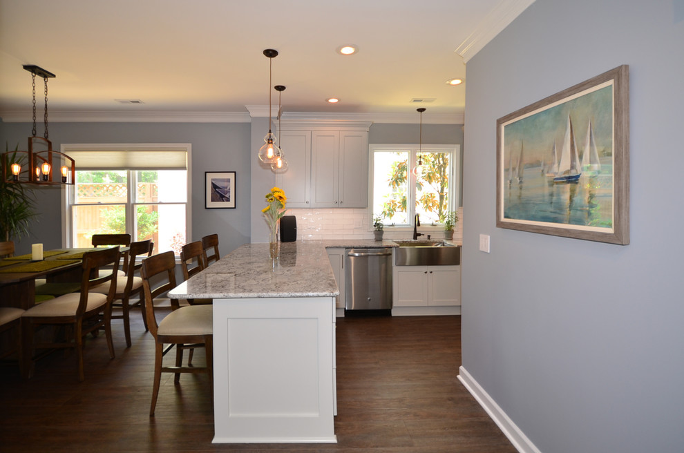 Inspiration for a mid-sized beach style galley eat-in kitchen in Charlotte with a farmhouse sink, shaker cabinets, grey cabinets, granite benchtops, white splashback, ceramic splashback, stainless steel appliances, vinyl floors, a peninsula, brown floor and multi-coloured benchtop.