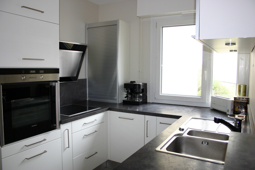 Idées déco pour cuisine ouverte in U With un évier 2 bacs, un placard à porte plane, des portes de placard blanches, un plan de travail en stratifié, une crédence noire, un électroménager en acier inoxydable, sol en stratifié, aucun îlot, un sol marron and plan de travail noir.