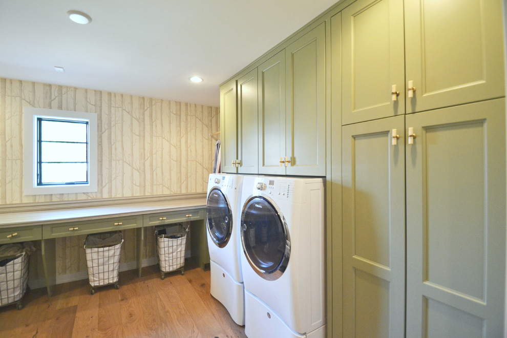 Mid-sized modern l-shaped dedicated laundry room in Indianapolis with recessed-panel cabinets, green cabinets, white walls, light hardwood floors and a side-by-side washer and dryer.