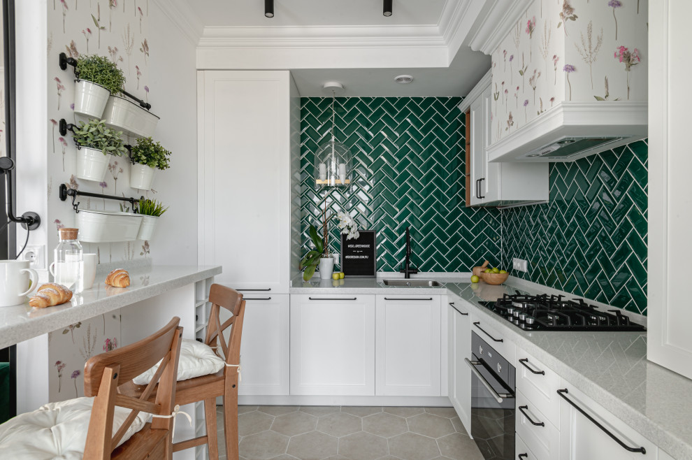 Example of a small danish l-shaped ceramic tile and beige floor open concept kitchen design in Other with an undermount sink, recessed-panel cabinets, white cabinets, solid surface countertops, green backsplash, ceramic backsplash, black appliances and white countertops