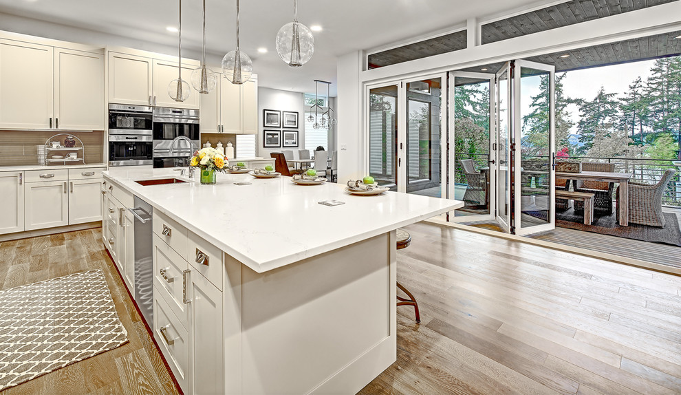 This is an example of a large transitional l-shaped eat-in kitchen in Seattle with an undermount sink, shaker cabinets, grey cabinets, quartz benchtops, grey splashback, glass tile splashback, stainless steel appliances, medium hardwood floors, with island, brown floor and white benchtop.