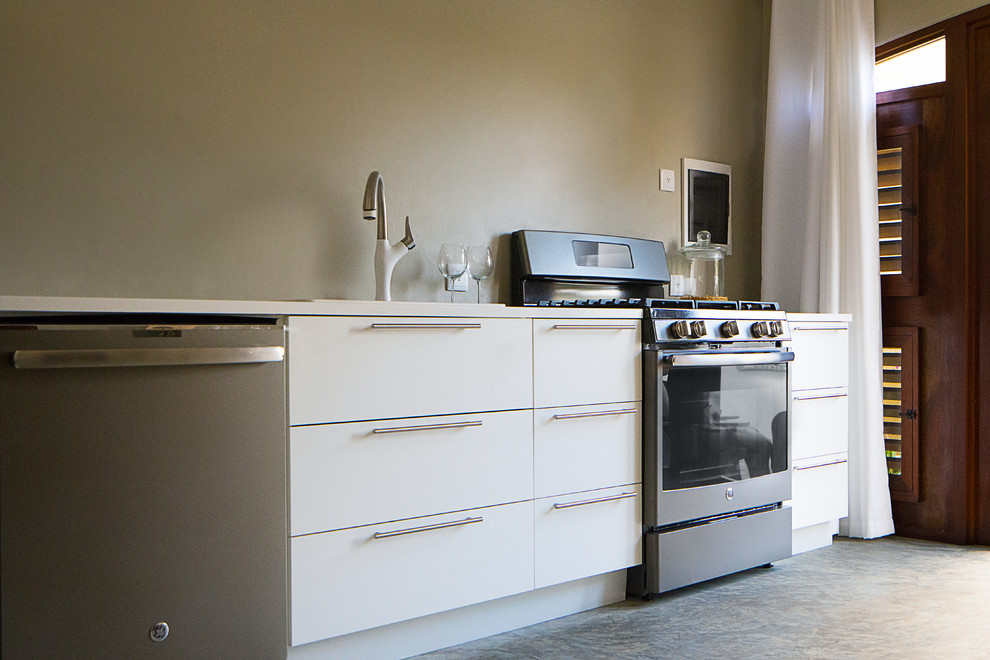 This is an example of a small tropical single-wall eat-in kitchen in Other with a drop-in sink, flat-panel cabinets, white cabinets, quartz benchtops, coloured appliances, concrete floors and grey floor.