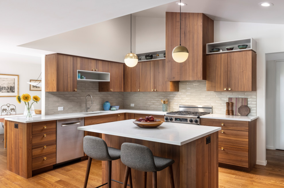Design ideas for a midcentury eat-in kitchen in Detroit with medium hardwood floors, with island, an undermount sink, flat-panel cabinets, medium wood cabinets, quartz benchtops, beige splashback, stainless steel appliances, brown floor, white benchtop and vaulted.