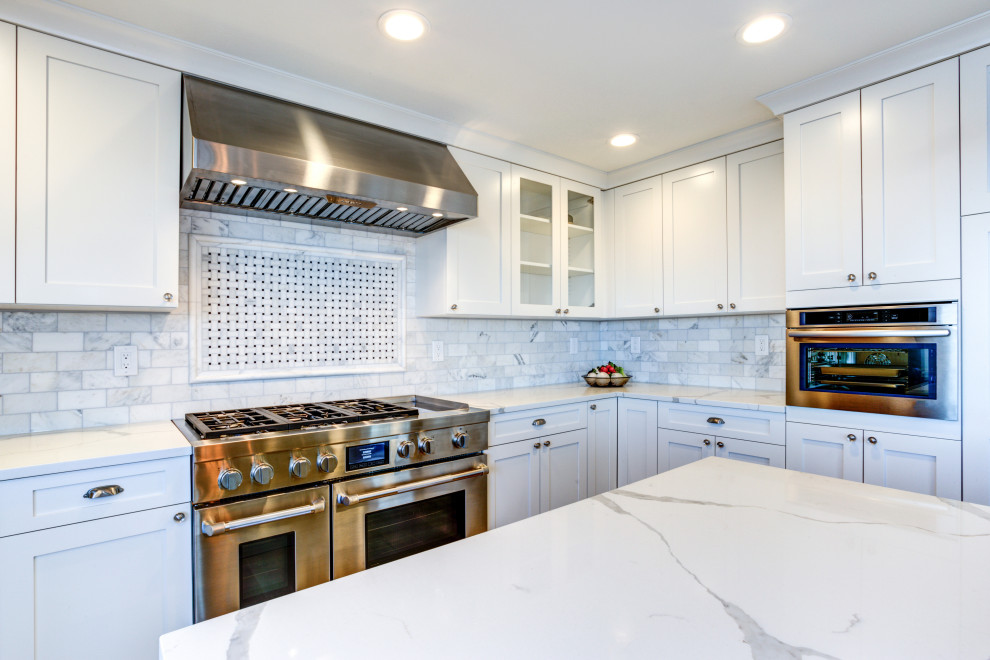 This is an example of a large modern galley eat-in kitchen in DC Metro with a farmhouse sink, shaker cabinets, white cabinets, quartz benchtops, white splashback, marble splashback, stainless steel appliances, medium hardwood floors, with island, brown floor and white benchtop.
