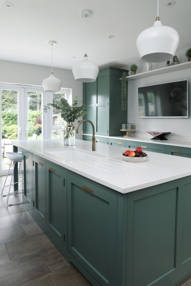 This is an example of a medium sized contemporary enclosed kitchen in Essex with a submerged sink, shaker cabinets, green cabinets, quartz worktops, white splashback, engineered quartz splashback, stainless steel appliances, vinyl flooring, an island, brown floors and white worktops.