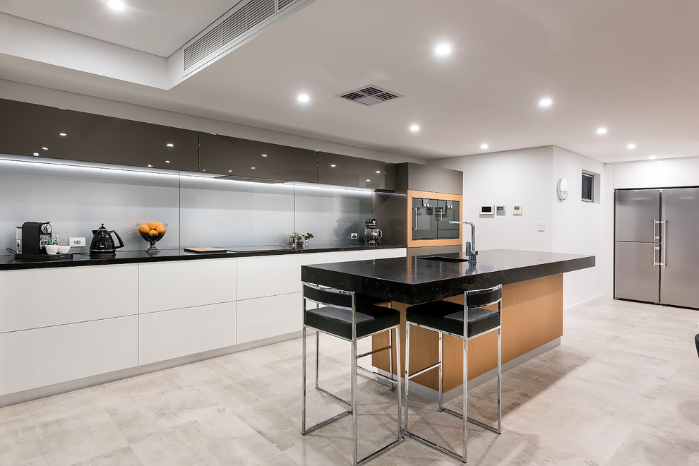Exemple d'une cuisine parallèle tendance de taille moyenne avec un plan de travail en quartz modifié, une crédence métallisée, une crédence en feuille de verre, un électroménager noir, îlot, un sol gris et plan de travail noir.