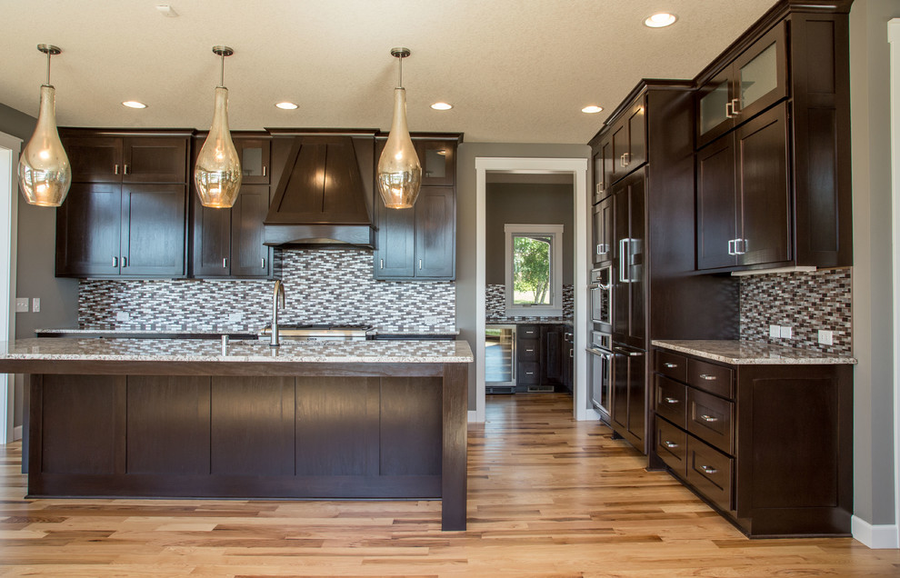 Photo of a transitional l-shaped eat-in kitchen in Minneapolis with a drop-in sink, shaker cabinets, dark wood cabinets, granite benchtops, multi-coloured splashback, ceramic splashback, stainless steel appliances, light hardwood floors and with island.