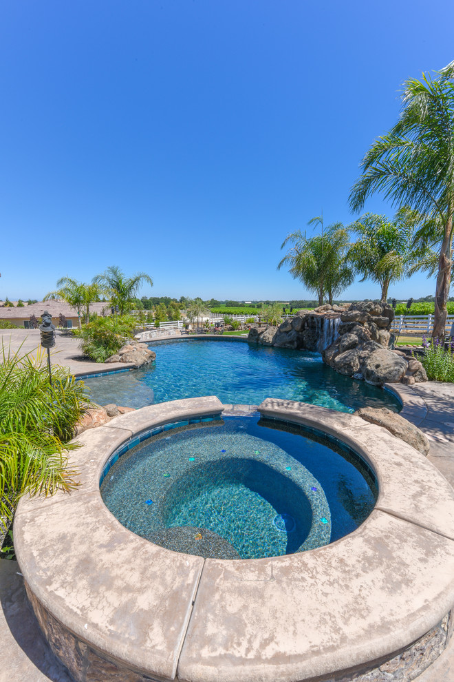 Large tropical backyard custom-shaped pool in Sacramento with a hot tub and natural stone pavers.