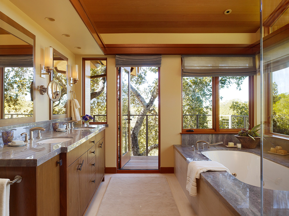 This is an example of an expansive contemporary master bathroom in San Francisco with flat-panel cabinets, dark wood cabinets, an undermount tub, limestone benchtops, beige walls, porcelain floors and an undermount sink.
