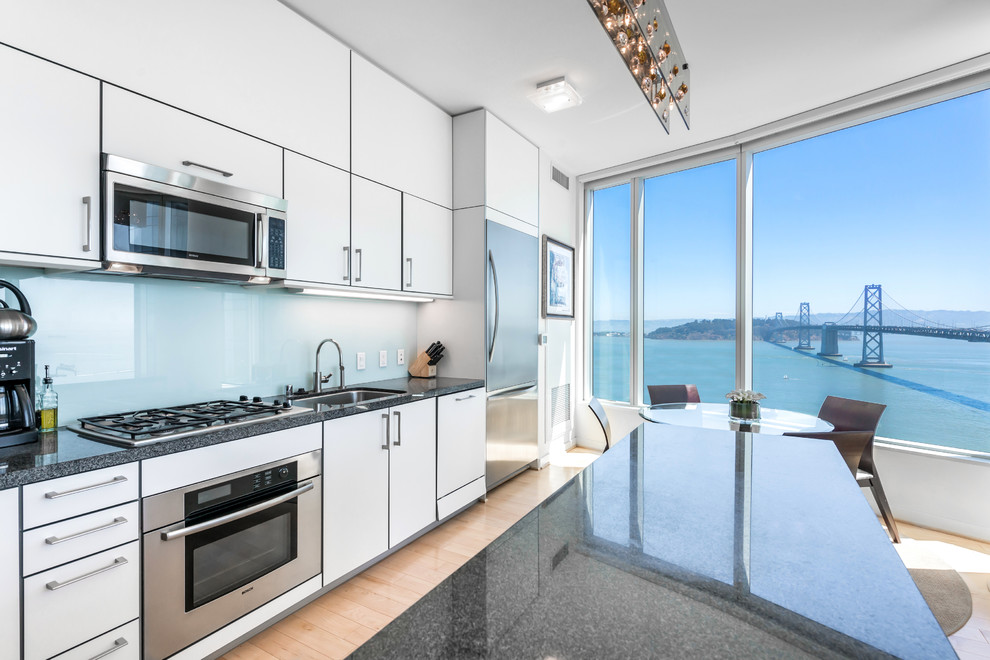 Eat-in kitchen - contemporary single-wall eat-in kitchen idea in San Francisco with an undermount sink, flat-panel cabinets, white cabinets, blue backsplash, glass sheet backsplash and stainless steel appliances