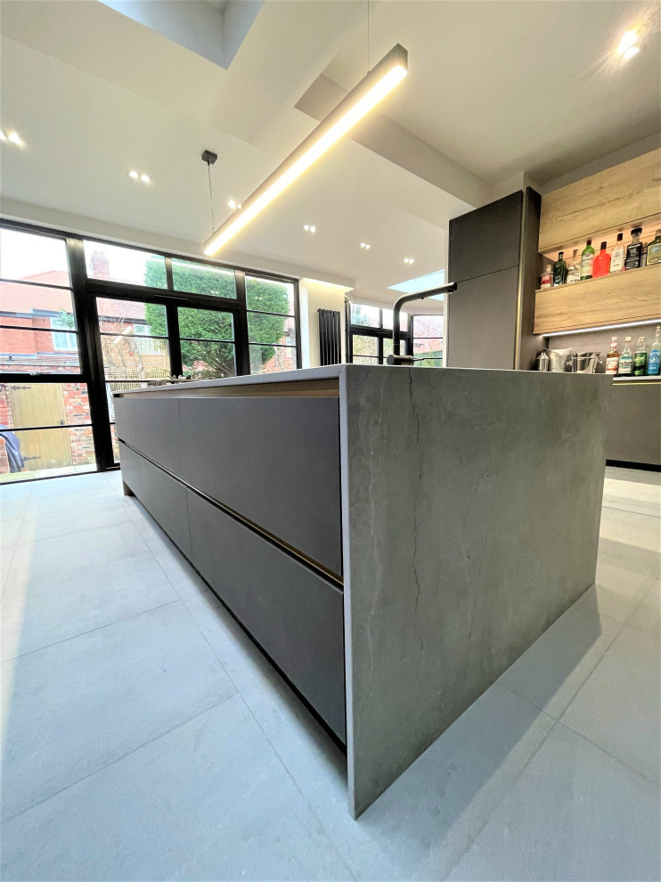 This is an example of a large contemporary single-wall kitchen in Other with a single-bowl sink, flat-panel cabinets, medium wood cabinets, solid surface benchtops, grey splashback, black appliances, ceramic floors, with island, grey floor and grey benchtop.