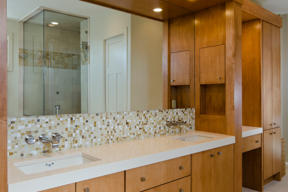 This is an example of a large contemporary master bathroom in Tampa with flat-panel cabinets, medium wood cabinets, an undermount tub, an alcove shower, beige tile, stone tile, beige walls, an undermount sink, solid surface benchtops and a hinged shower door.