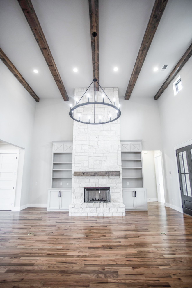 This is an example of a large country open concept living room in Dallas with grey walls, medium hardwood floors, a standard fireplace, a stone fireplace surround, no tv and brown floor.