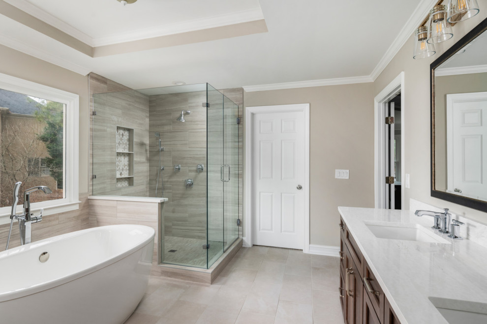 Inspiration for a large transitional master bathroom in Atlanta with shaker cabinets, brown cabinets, a freestanding tub, a double shower, a one-piece toilet, beige tile, porcelain tile, beige walls, porcelain floors, a drop-in sink, engineered quartz benchtops, beige floor, a hinged shower door and white benchtops.