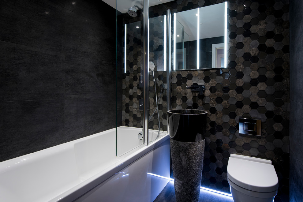 Photo of a small contemporary kids bathroom in London with recessed-panel cabinets, black cabinets, a drop-in tub, a shower/bathtub combo, a wall-mount toilet, black tile, porcelain tile, black walls, porcelain floors and a vessel sink.