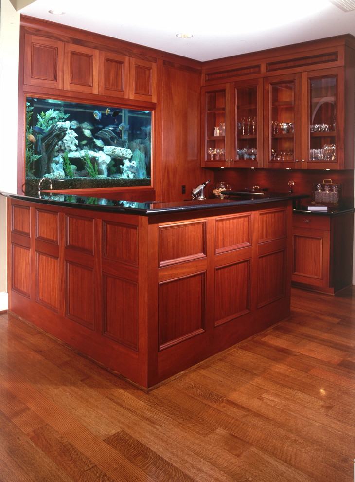This is an example of a mid-sized traditional u-shaped wet bar in Houston with beaded inset cabinets, dark wood cabinets, quartz benchtops, brown splashback, timber splashback, medium hardwood floors and brown floor.
