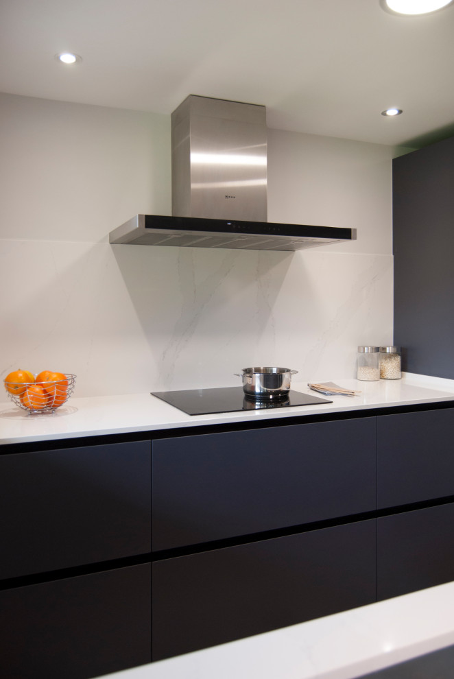 Mid-sized modern single-wall open plan kitchen in Bilbao with an undermount sink, flat-panel cabinets, grey cabinets, quartz benchtops, white splashback, engineered quartz splashback, black appliances, a peninsula and white benchtop.