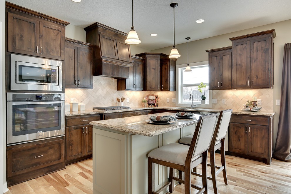 Design ideas for a large arts and crafts l-shaped open plan kitchen in Minneapolis with an undermount sink, flat-panel cabinets, medium wood cabinets, granite benchtops, beige splashback, cement tile splashback, stainless steel appliances, light hardwood floors and with island.