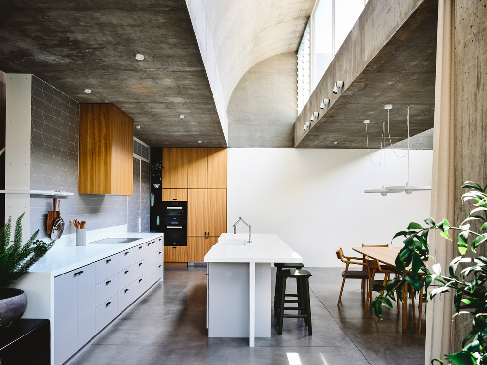 Contemporary galley open plan kitchen in Melbourne with a double-bowl sink, flat-panel cabinets, grey cabinets, grey splashback, black appliances, concrete floors, with island and grey floor.
