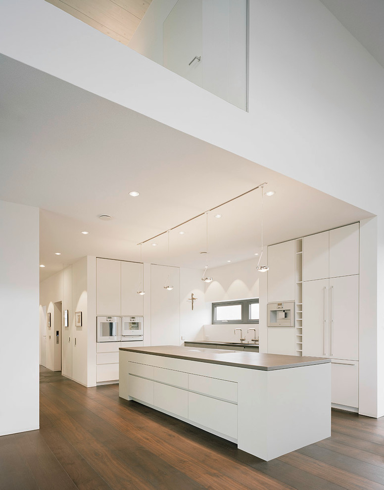 Design ideas for an expansive contemporary l-shaped open plan kitchen in Munich with a double-bowl sink, flat-panel cabinets, white cabinets, white splashback, dark hardwood floors, with island and stainless steel appliances.