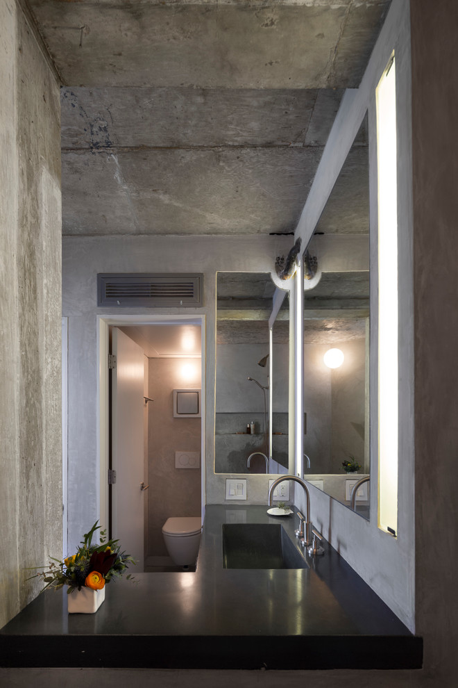 Photo of a small industrial master bathroom in Austin with an integrated sink, flat-panel cabinets, dark wood cabinets, concrete benchtops, an undermount tub, an open shower and a wall-mount toilet.