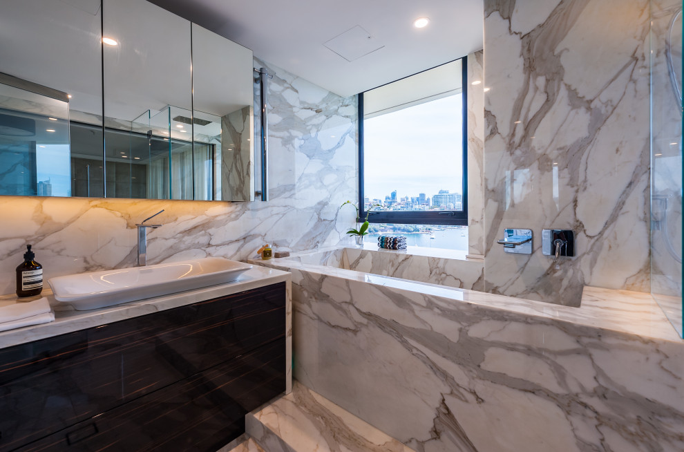 Design ideas for a mid-sized contemporary master wet room bathroom in Sydney with furniture-like cabinets, dark wood cabinets, a wall-mount toilet, white tile, marble, multi-coloured walls, marble floors, a vessel sink, marble benchtops, multi-coloured floor, an open shower and white benchtops.
