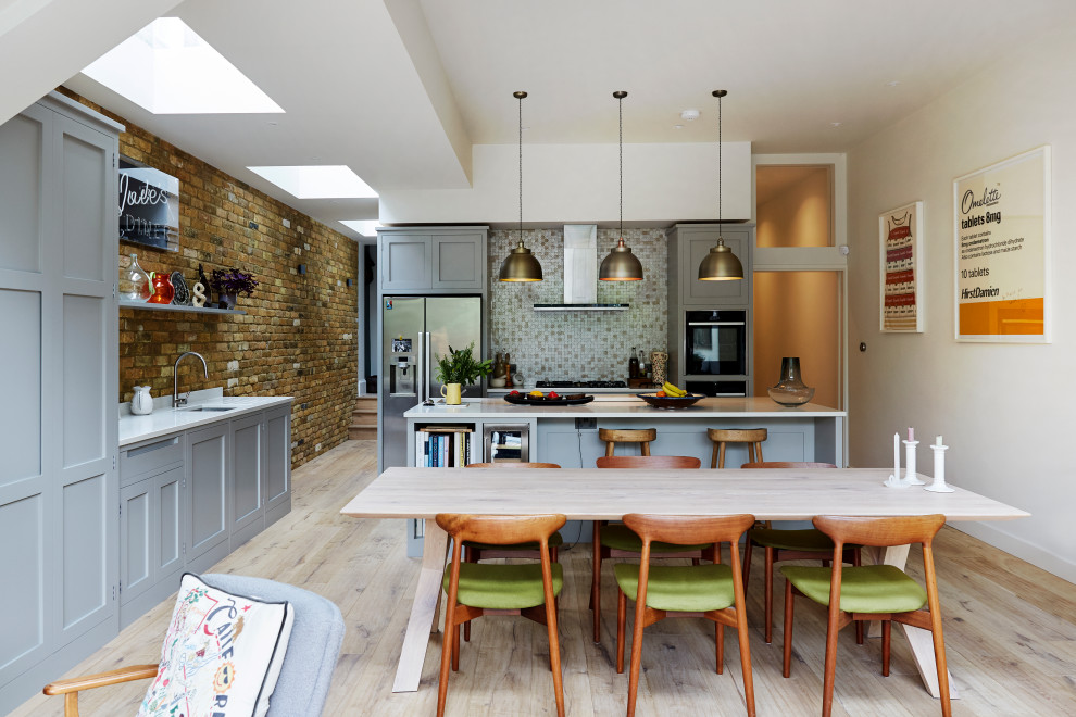Photo of a classic u-shaped kitchen/diner in London with a submerged sink, shaker cabinets, grey cabinets, engineered stone countertops, stainless steel appliances, medium hardwood flooring, an island, brown floors and white worktops.