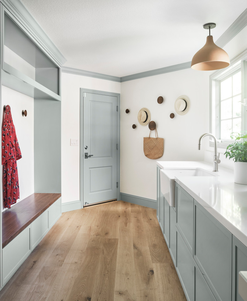 Inspiration for a large transitional galley light wood floor utility room remodel in San Francisco with a farmhouse sink, shaker cabinets, gray cabinets, quartz countertops, white backsplash, quartz backsplash, white walls, a side-by-side washer/dryer and white countertops