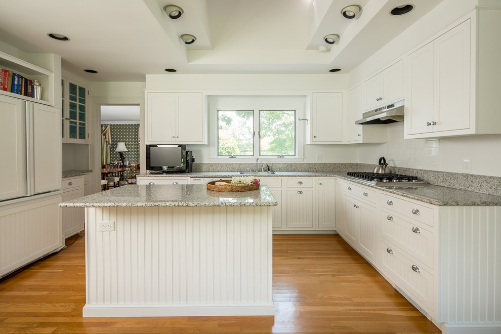 Design ideas for a mid-sized traditional l-shaped separate kitchen in New York with a drop-in sink, shaker cabinets, white cabinets, granite benchtops, white splashback, subway tile splashback, panelled appliances, medium hardwood floors, with island and brown floor.