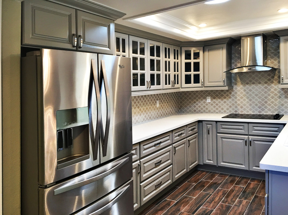 Example of a mid-sized transitional u-shaped medium tone wood floor eat-in kitchen design in Orange County with raised-panel cabinets, gray cabinets, quartz countertops, a peninsula, a double-bowl sink, brown backsplash, mosaic tile backsplash and stainless steel appliances