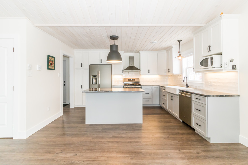 Kitchen - mid-sized l-shaped vinyl floor and brown floor kitchen idea with a farmhouse sink, recessed-panel cabinets, white cabinets, laminate countertops, white backsplash, subway tile backsplash, stainless steel appliances, an island and multicolored countertops