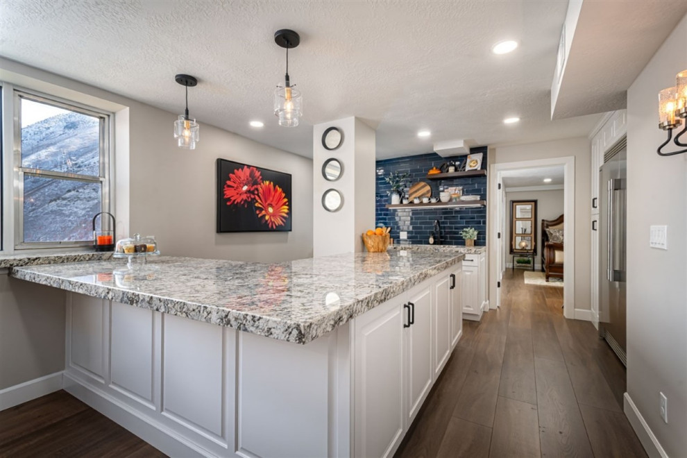 Photo of a mid-sized transitional u-shaped eat-in kitchen in Salt Lake City with an undermount sink, raised-panel cabinets, white cabinets, granite benchtops, blue splashback, subway tile splashback, stainless steel appliances, medium hardwood floors, brown floor and blue benchtop.