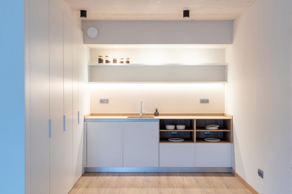 Diseño de cocinas en U minimalista abierto con armarios con paneles lisos, puertas de armario grises, suelo de madera en tonos medios, península y suelo marrón