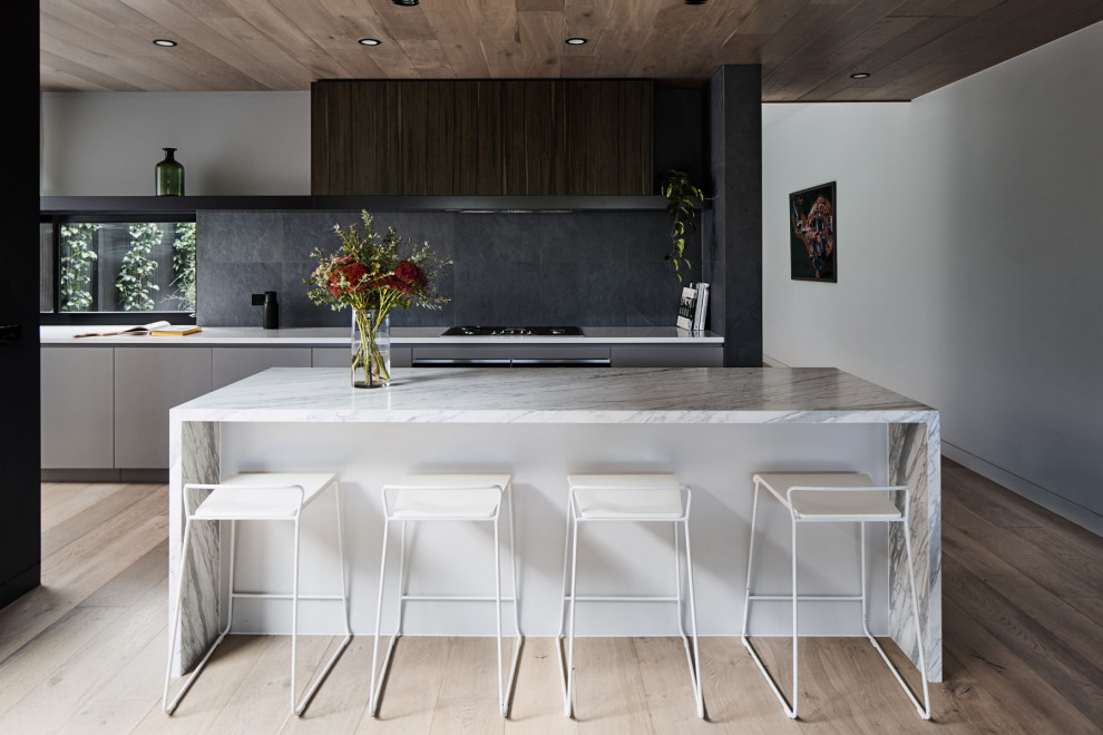 Contemporary galley kitchen in Melbourne with flat-panel cabinets, grey cabinets, black splashback, light hardwood floors, with island, beige floor and white benchtop.