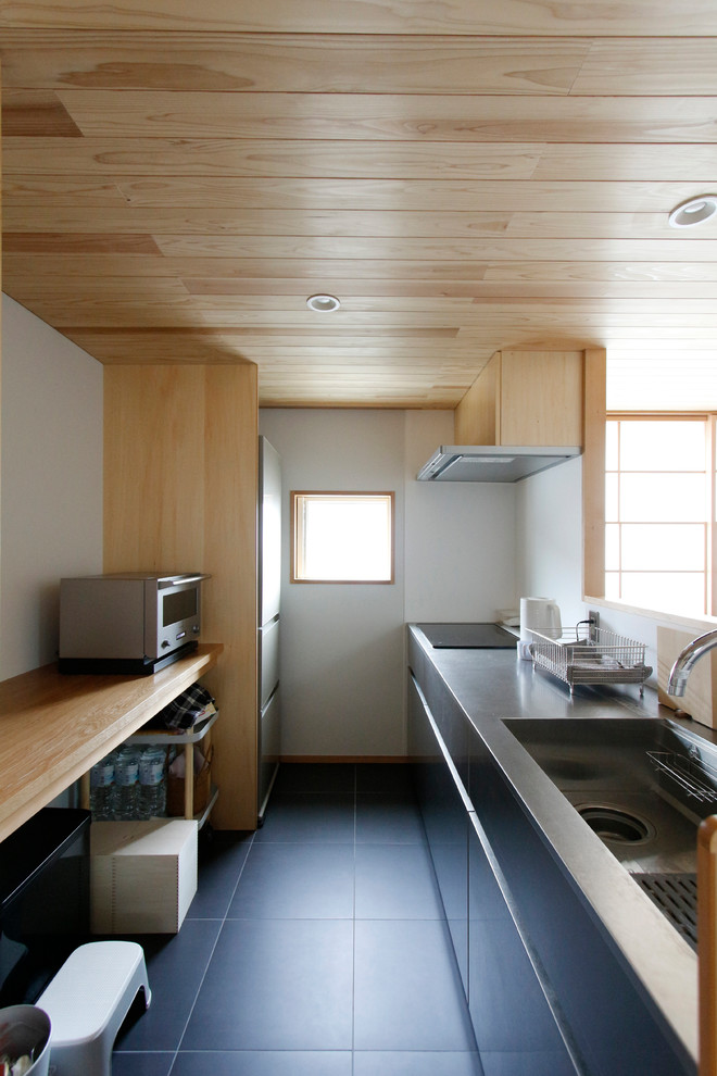 Photo of an asian single-wall kitchen in Tokyo Suburbs with an integrated sink, flat-panel cabinets, black cabinets, white splashback, a peninsula, black floor and brown benchtop.
