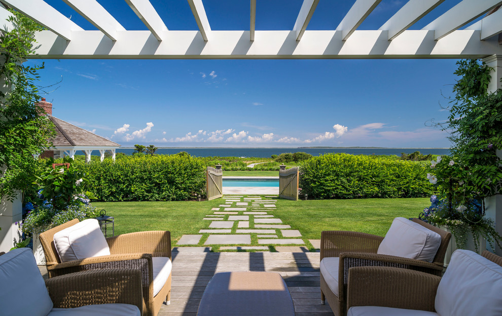 This is an example of an expansive beach style backyard patio in Boston with decking and a pergola.