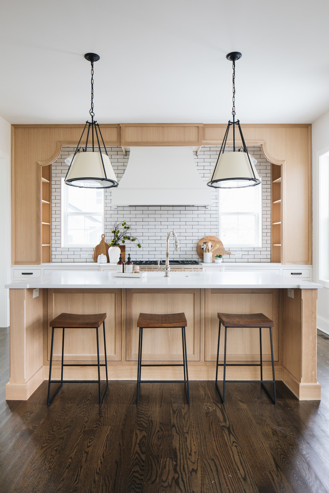 This is an example of a transitional galley kitchen in Chicago with shaker cabinets, light wood cabinets, white splashback, subway tile splashback, dark hardwood floors, with island, brown floor and white benchtop.