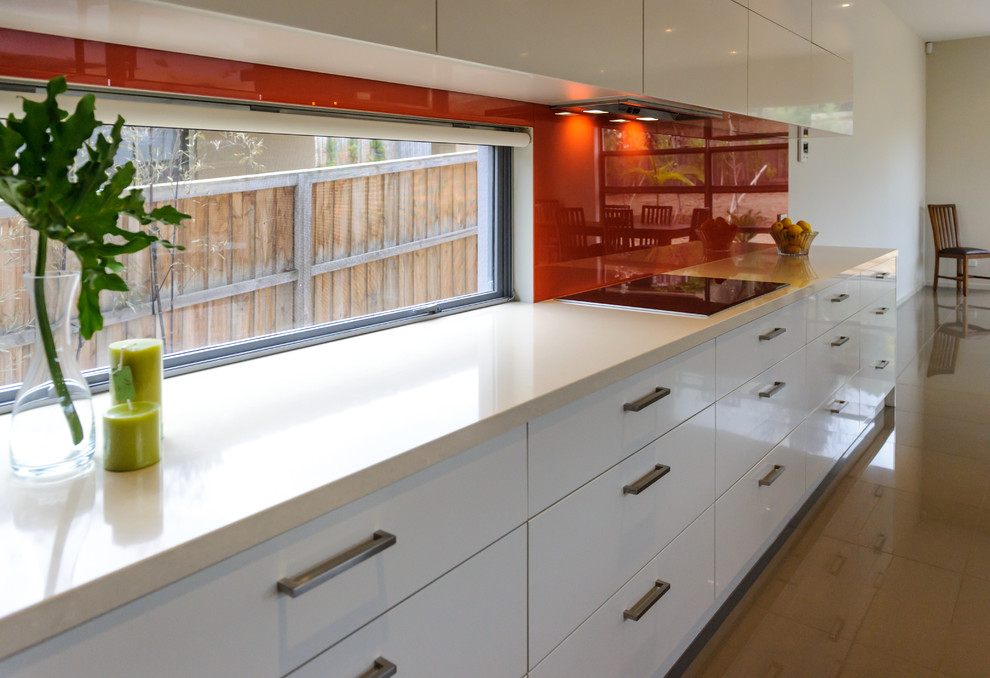 Design ideas for a large contemporary open plan kitchen in Melbourne with an undermount sink, flat-panel cabinets, white cabinets, glass benchtops, red splashback, glass sheet splashback, porcelain floors and with island.