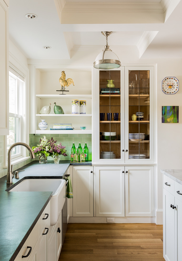 Inspiration for a transitional l-shaped kitchen in Boston with a farmhouse sink, glass-front cabinets, white cabinets, medium hardwood floors, with island, green splashback and subway tile splashback.