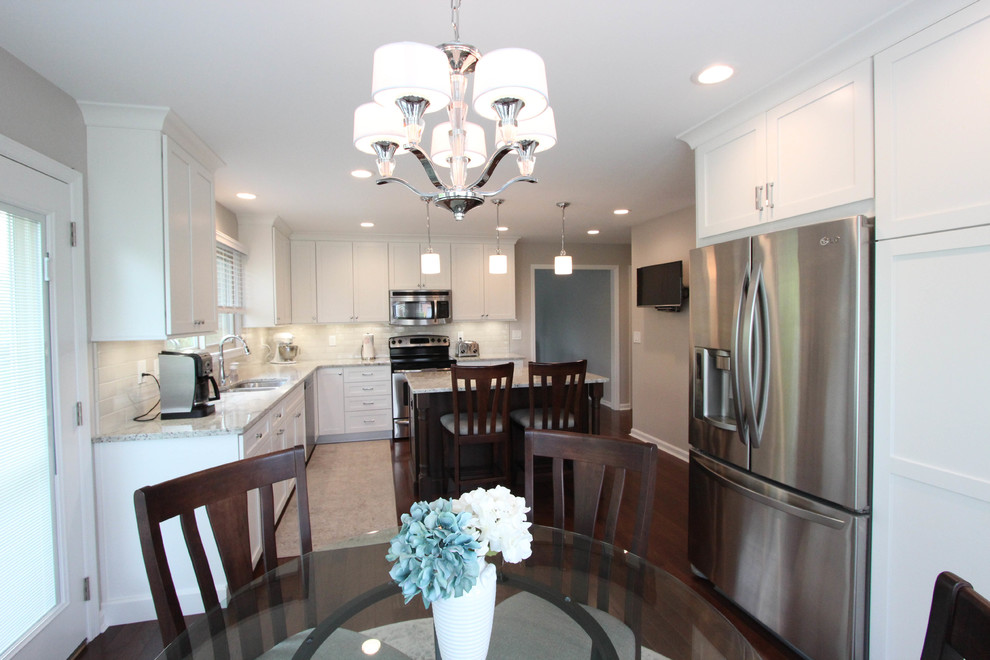 Example of a mid-sized transitional l-shaped dark wood floor and brown floor enclosed kitchen design in Cincinnati with an undermount sink, shaker cabinets, white cabinets, granite countertops, beige backsplash, porcelain backsplash, stainless steel appliances, an island and white countertops