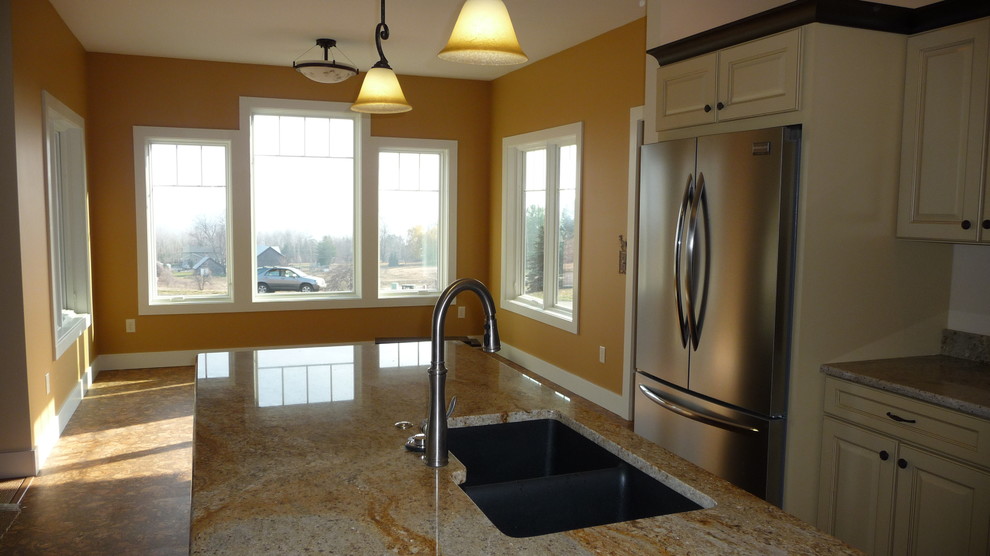 Example of a transitional l-shaped cork floor and brown floor open concept kitchen design with a double-bowl sink, raised-panel cabinets, yellow cabinets, granite countertops, white backsplash, mosaic tile backsplash, stainless steel appliances and an island