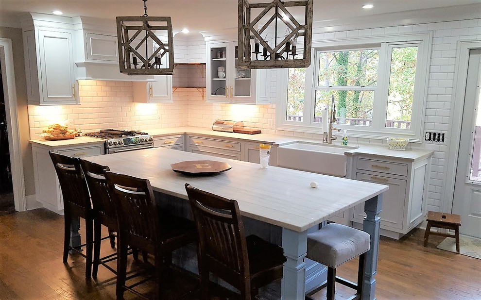This is an example of a large transitional l-shaped separate kitchen in Miami with white splashback, subway tile splashback, with island, a farmhouse sink, recessed-panel cabinets, white cabinets, marble benchtops, stainless steel appliances, medium hardwood floors, brown floor and white benchtop.